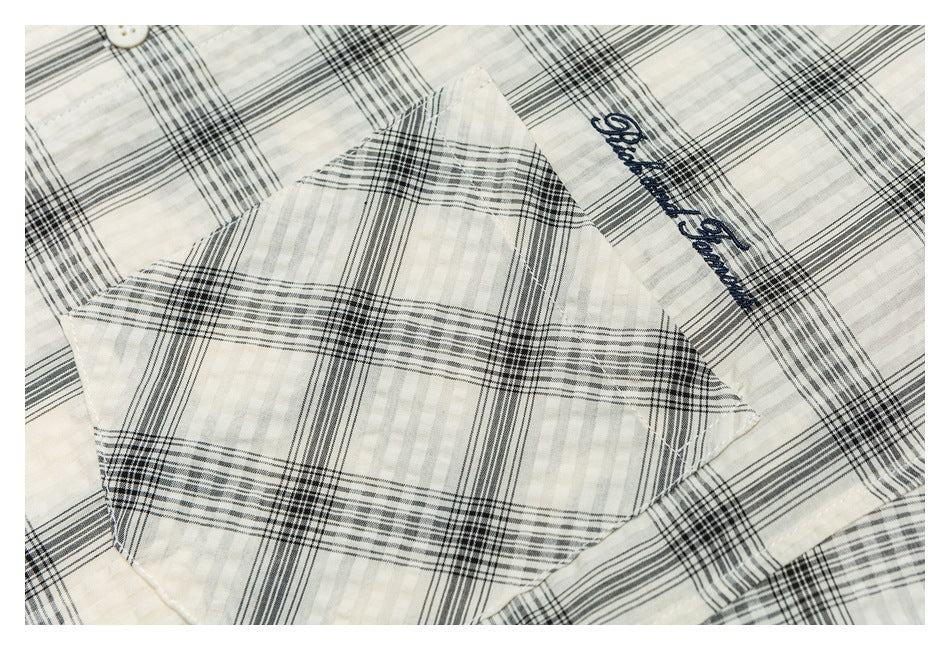 Close-up of the ivory plaid shirt's chest pocket and dark script embroidery.