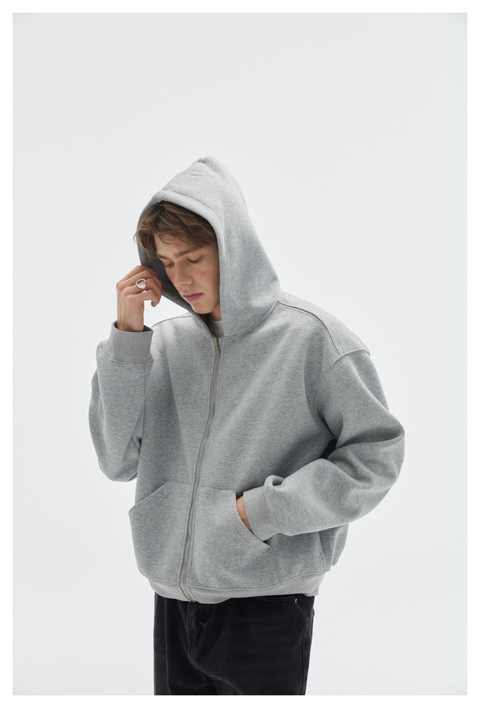 Closer view of a model wearing a light gray hooded zip-up sweatshirt with front pockets and ribbed cuffs.