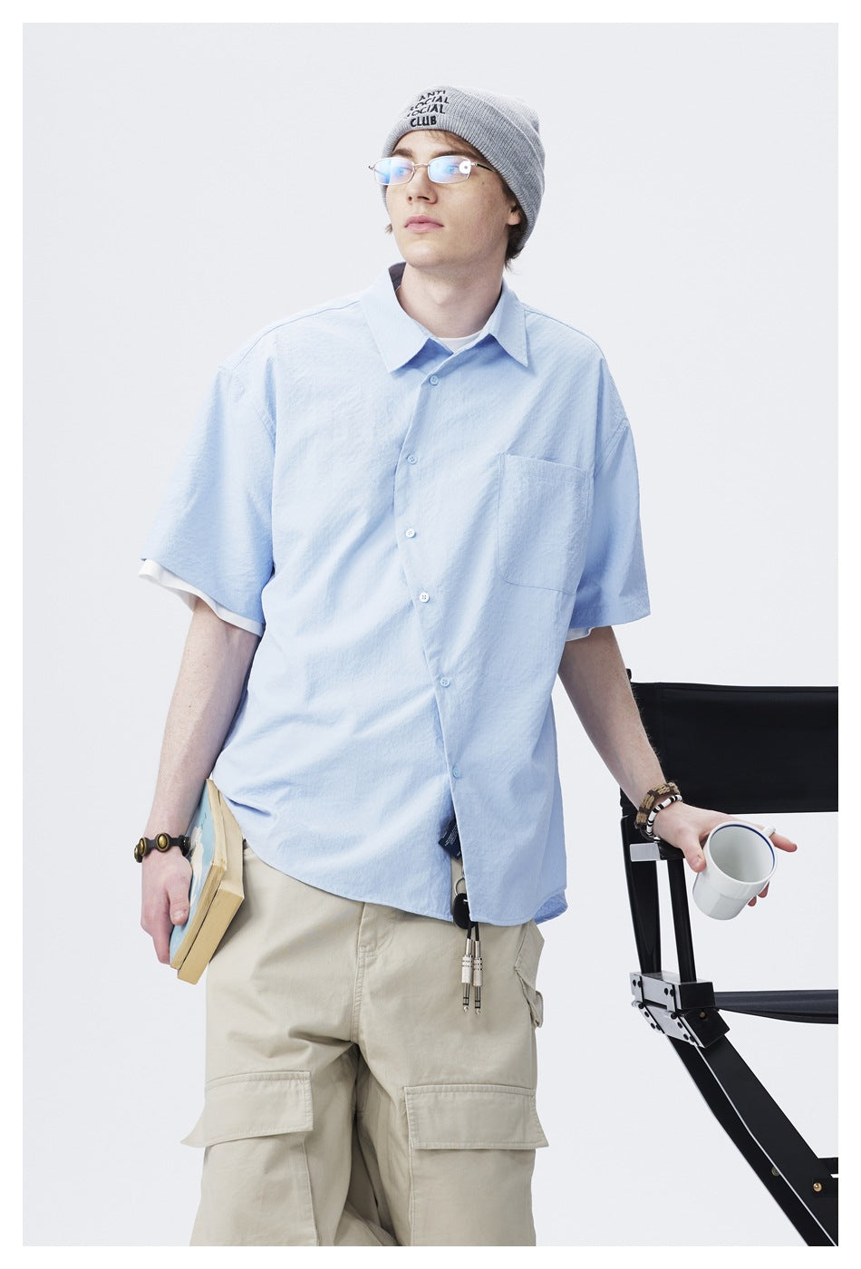 Model wearing a light blue short-sleeve button-up shirt with a chest pocket, shown from the front.