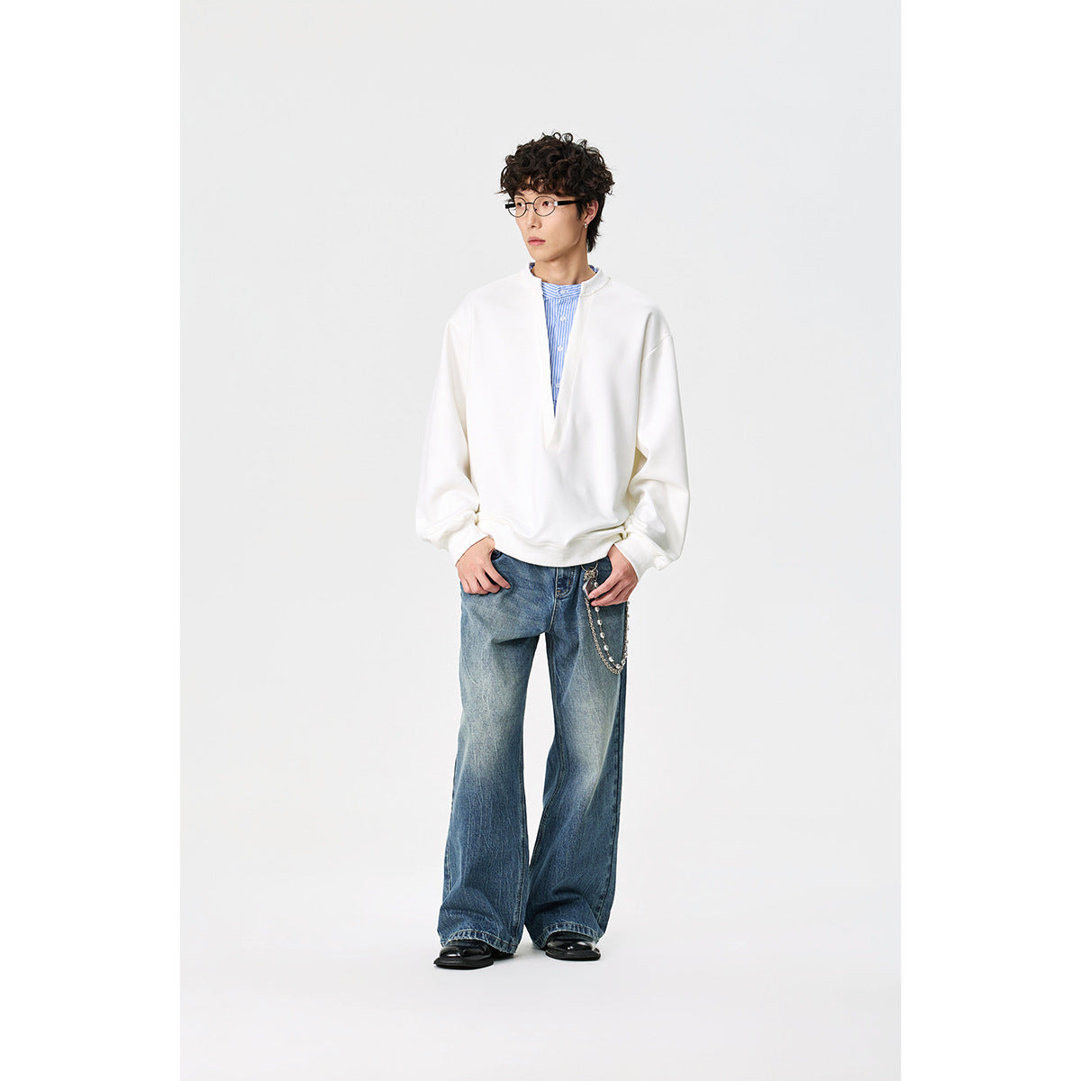 Model wearing a white oversized pullover with a split V neckline over a blue striped shirt.