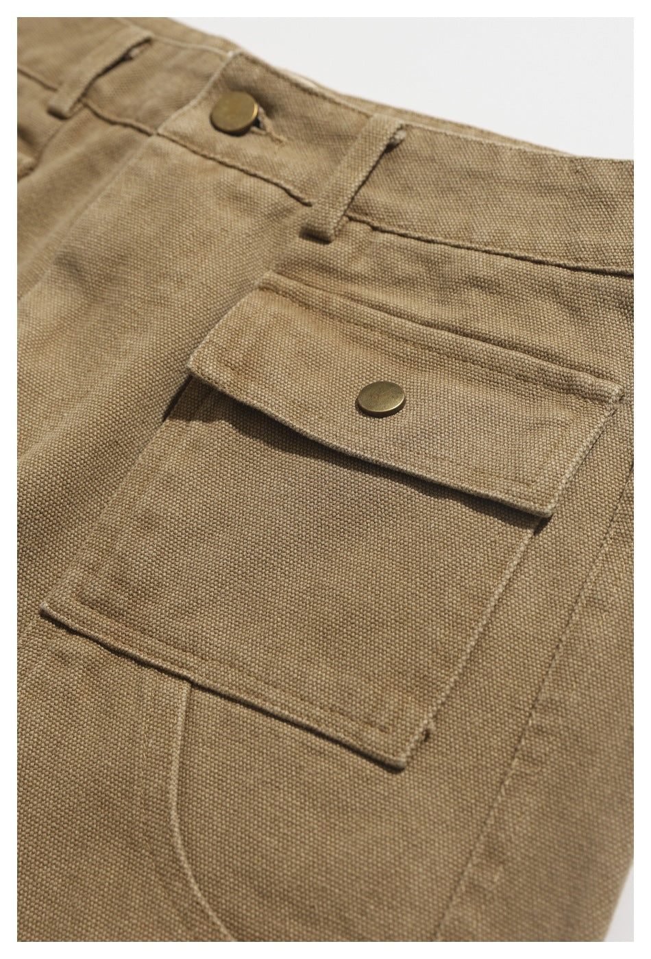 Close-up of tan utility trousers showing a large front patch pocket with a brass-tone snap flap.