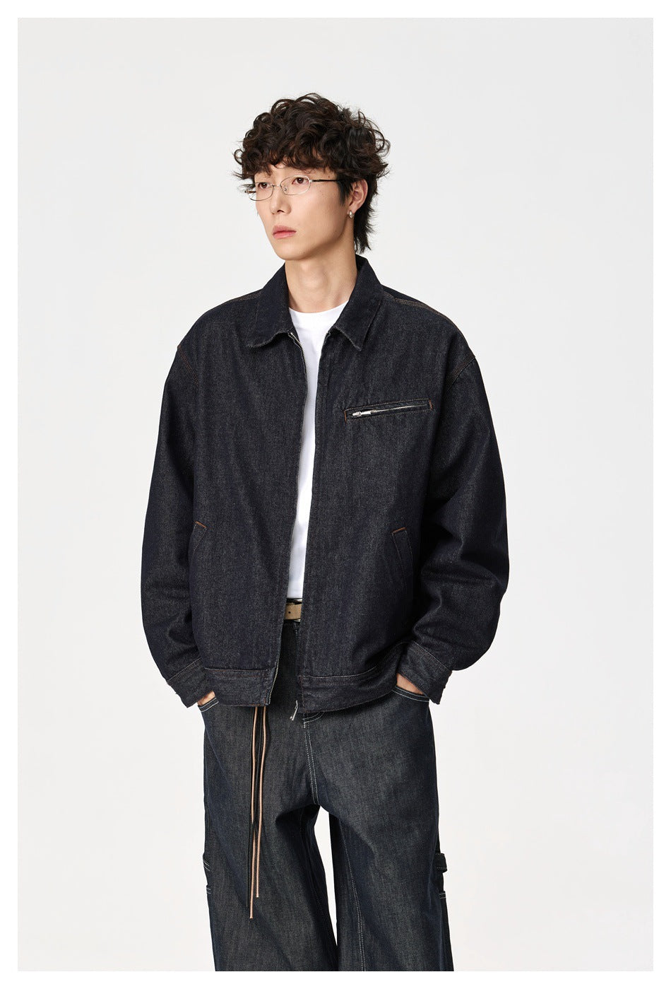 Model wearing dark indigo denim zip jacket over a white tee with dark jeans, hands in pockets