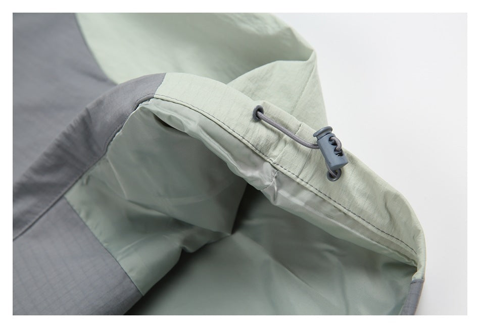 Close-up of a pale sage and gray color-block garment edge with a gray drawcord and toggle.