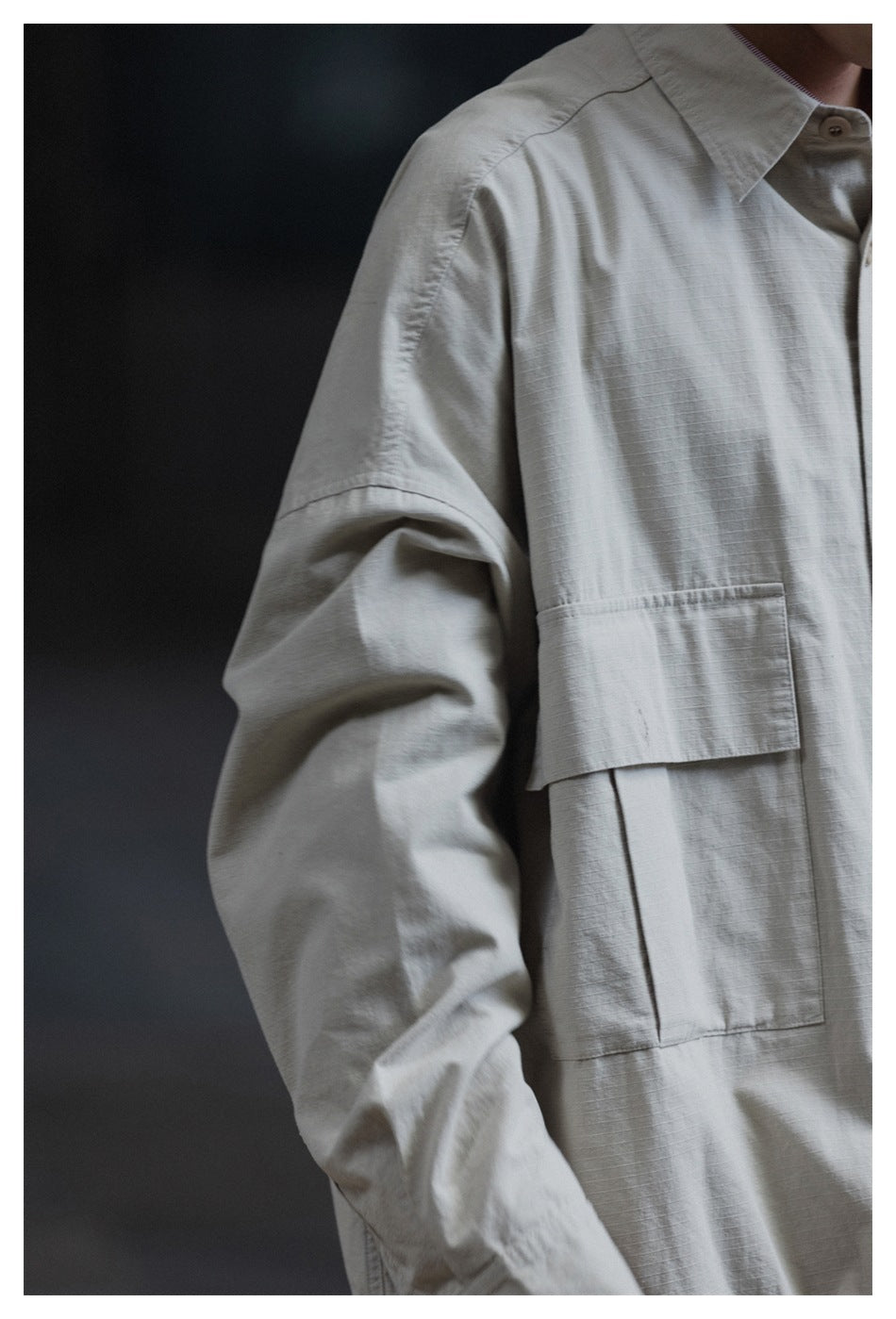 Close-up of the light gray jacket's sleeve, shoulder seam, and large front flap pocket.