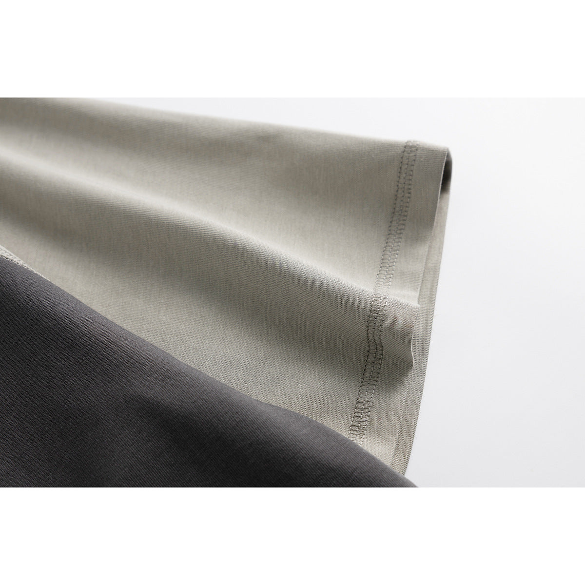 Close-up of a light gray T-shirt sleeve hem and overlock stitching beside the charcoal shirt body.