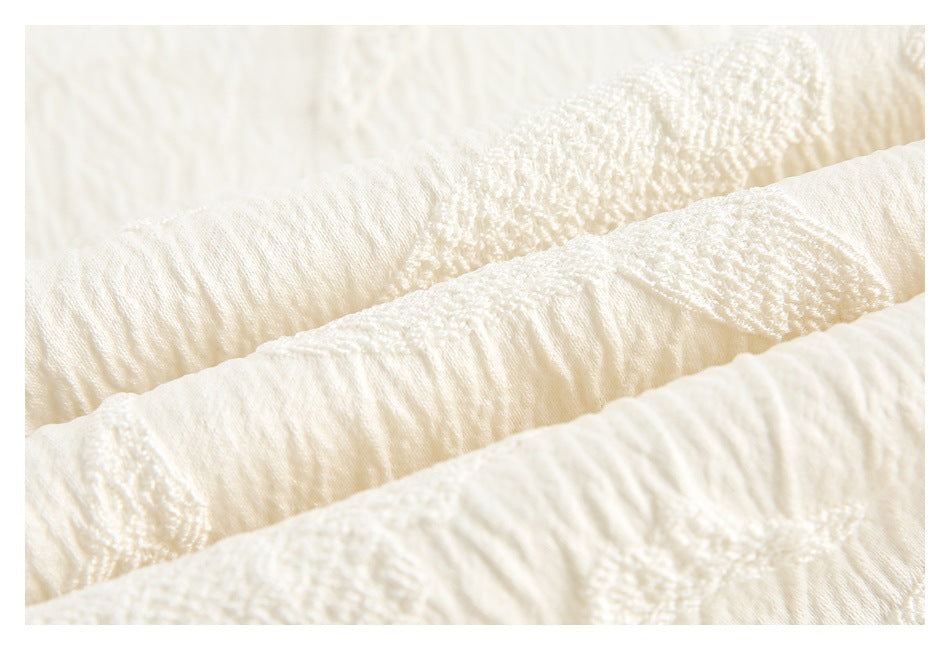 Macro view of ivory fabric showing its crinkled texture and raised decorative stitching.