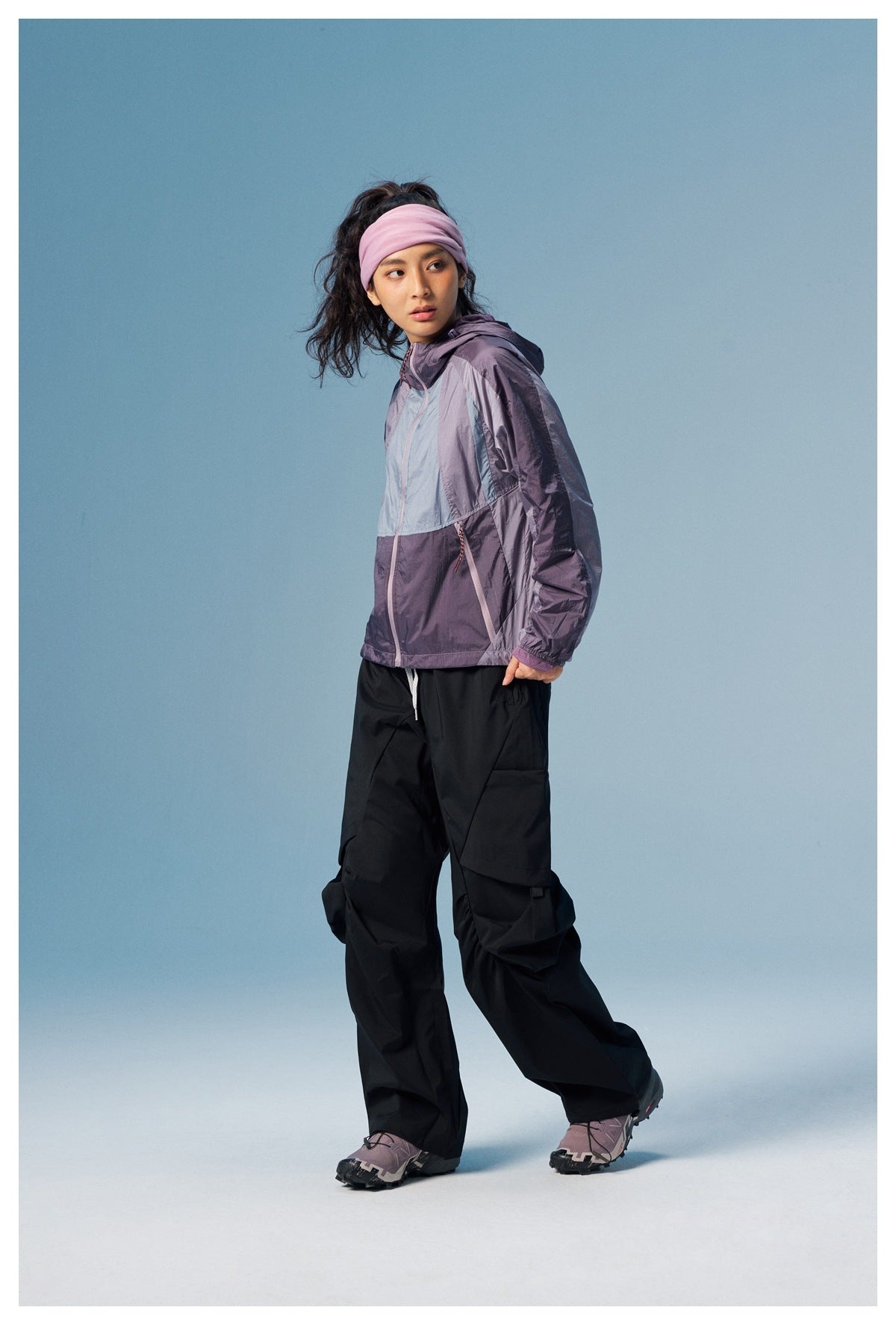 Model in a purple and pale-blue color-block hooded jacket, shown at an angle with black cargo pants.