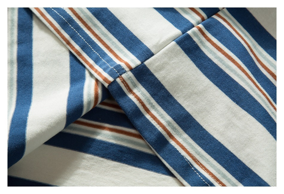 Close-up of a striped garment with blue, cream, pale green, and rust bands meeting at a stitched seam.