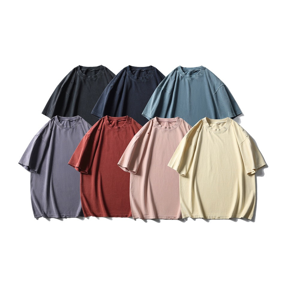 Seven plain oversized crew-neck T-shirts arranged together in black, navy, blue-gray, lavender, red, pink, and pale yellow.