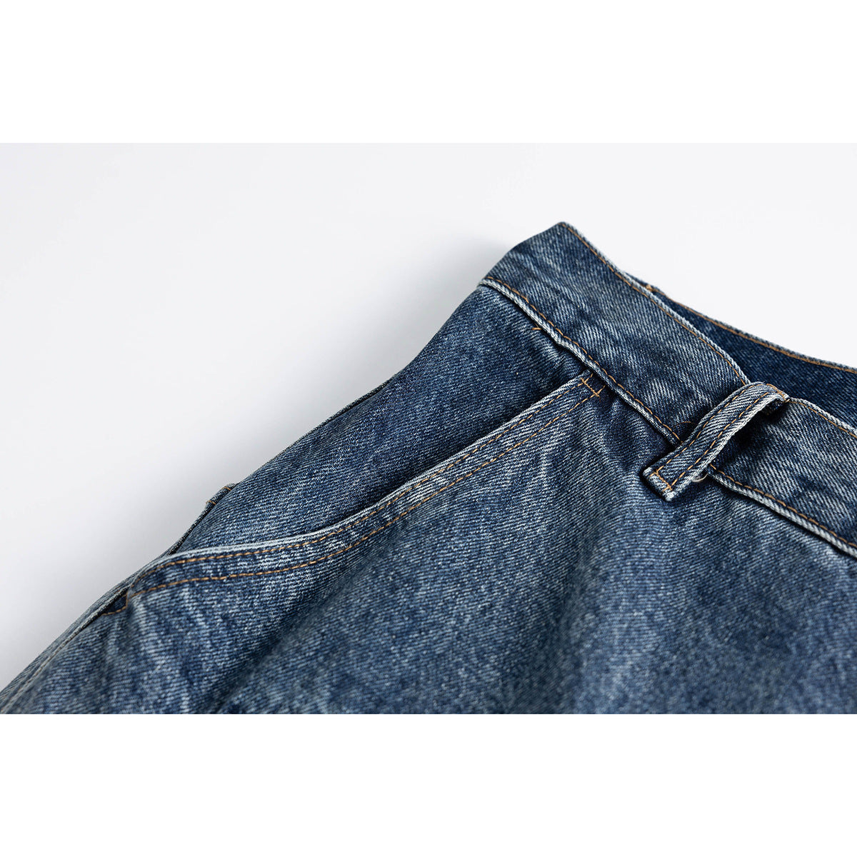 Close-up of blue washed jeans showing a curved front pocket, waistband and belt loop.