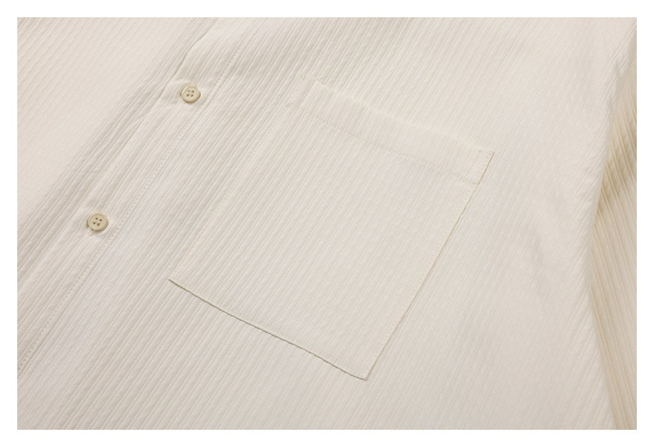 Close-up of a square chest pocket, buttons, and fine vertical ribbing on the ivory shirt.