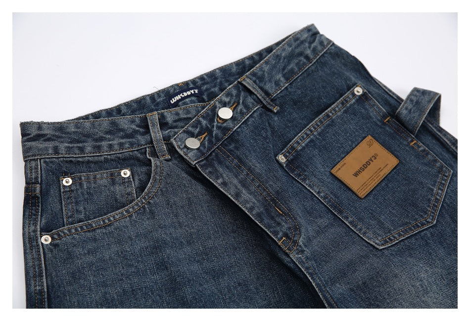 Close-up of dark blue washed jeans showing the waistband, button fly, front pockets and brown branded patch.