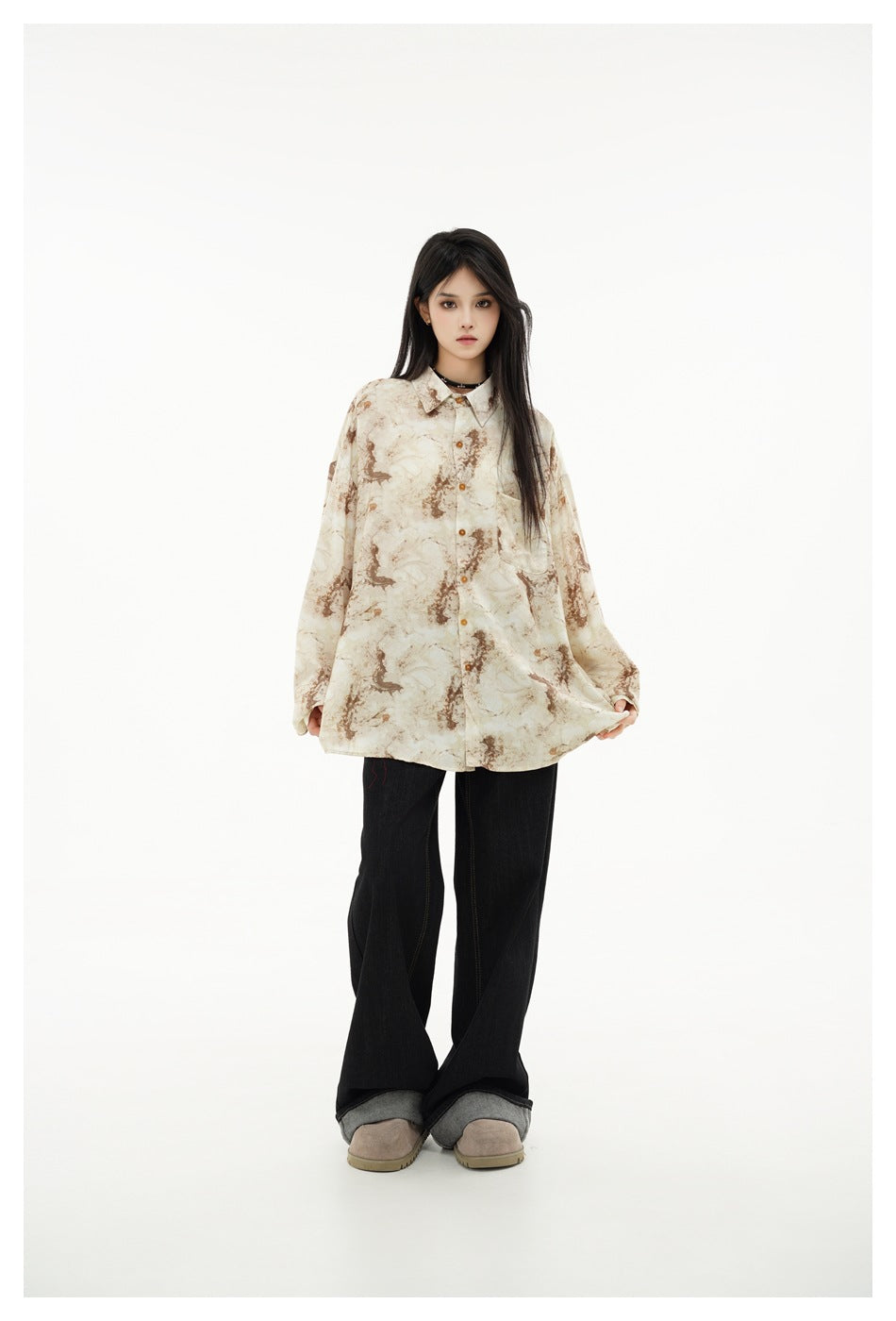 Model wearing loose marbled beige and brown long-sleeve shirt, holding the hem, with black flared jeans