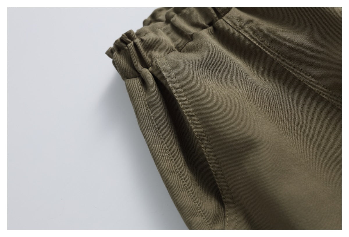 Close-up of olive-brown trousers showing the elastic waistband and stitched side pocket opening.