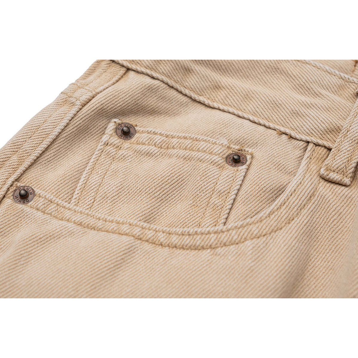 Close-up of a small front pocket with metal rivets on beige pants.