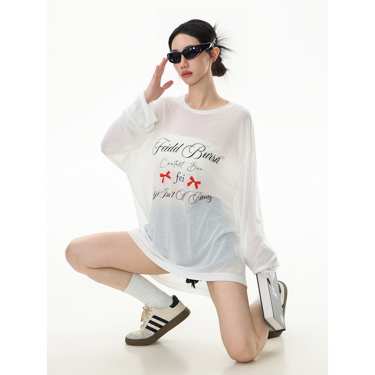 Model wearing an oversized sheer white long-sleeve tee with black script and red bow graphics, front view.