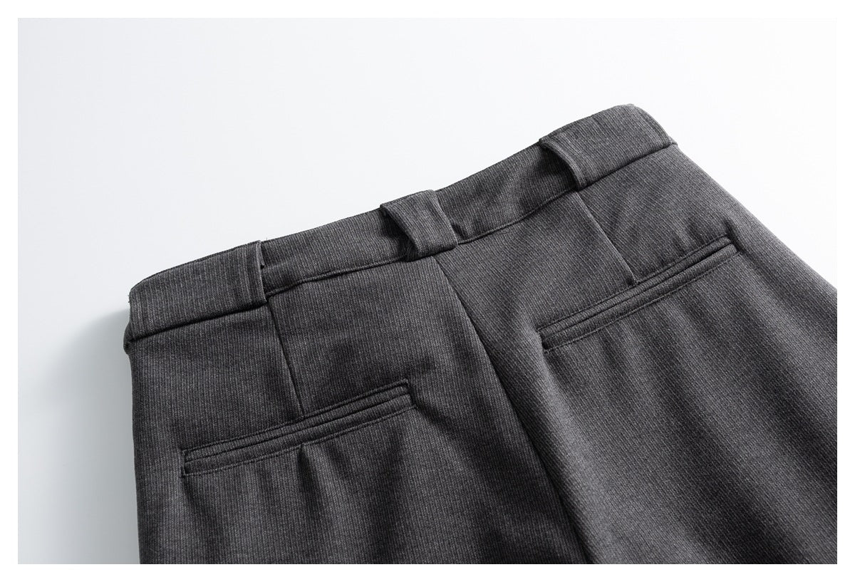Close-up of charcoal gray trousers showing the waistband, belt loops, and two rear welt pockets.