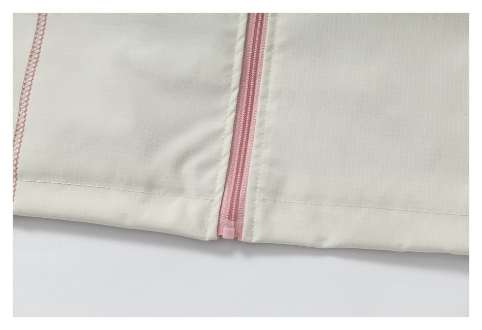 Close-up of a pink zipper at the hem of a cream garment, with pink overlock stitching.