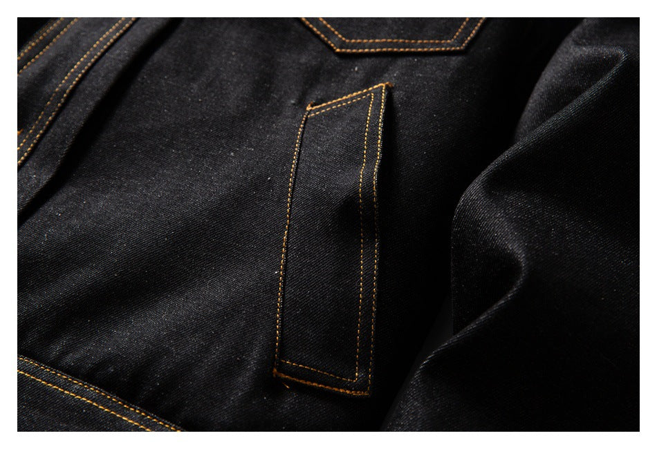 Close-up of a narrow stitched tab on black denim beside a sleeve, with golden-brown seams.