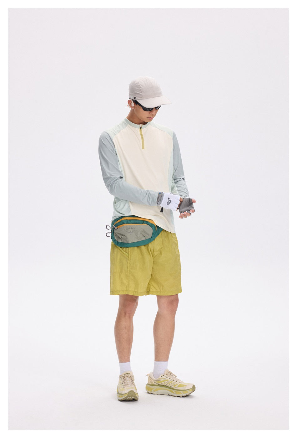 Full-length view of a man wearing a cream and pale sage quarter-zip top with yellow shorts.