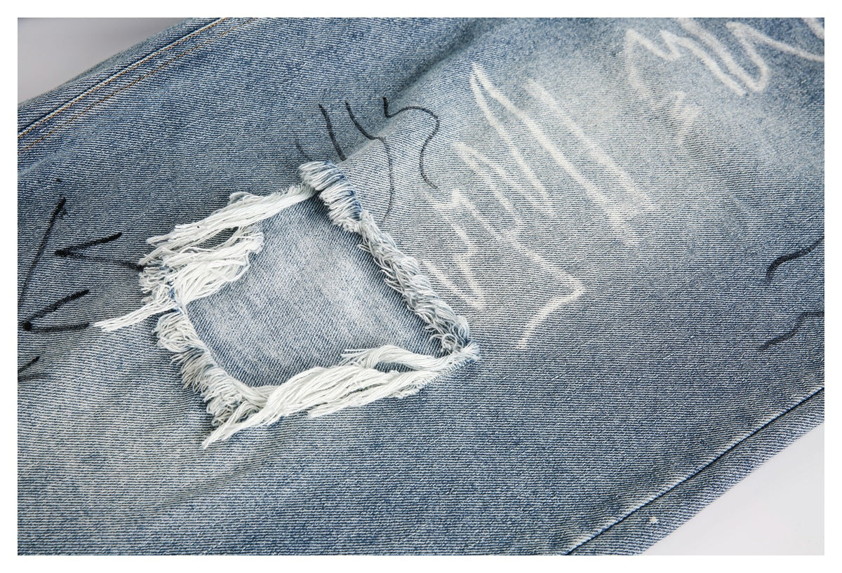 Close-up of a distressed, frayed denim patch with abstract dark markings and pale wash patterns.
