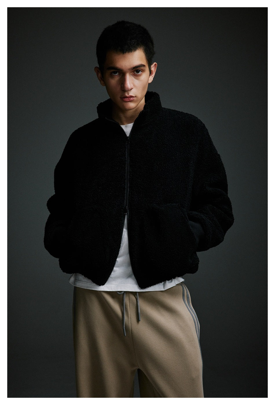 Model wearing a black textured zip-up jacket over a white shirt and taupe drawstring pants.