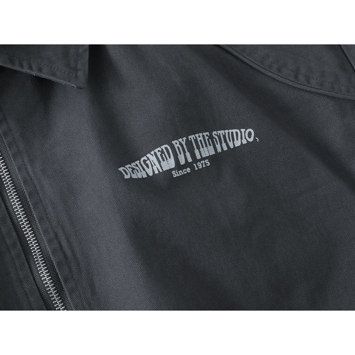 Close-up of a charcoal jacket chest showing the white printed text “Designed by the Studio, Since 1975.”