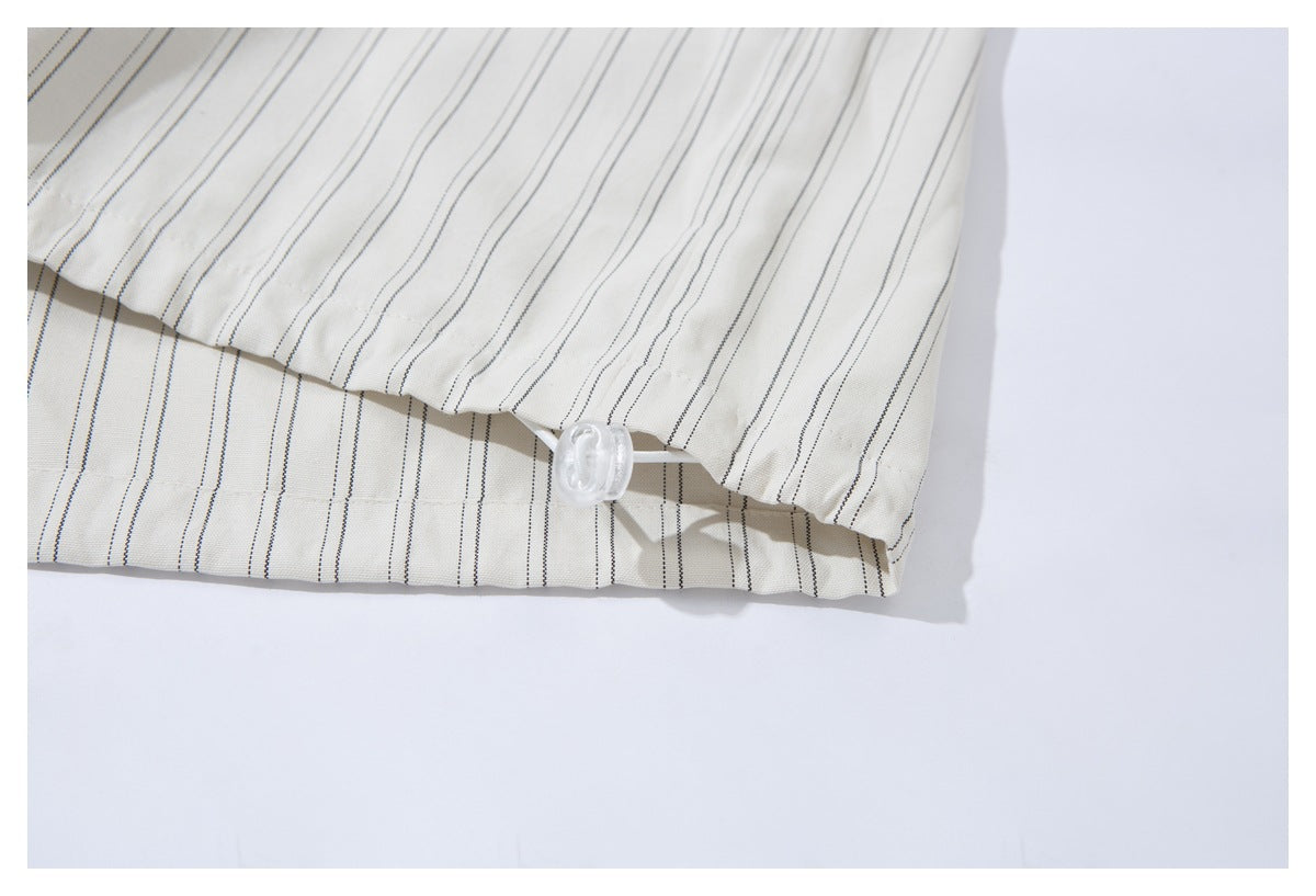 Close-up of the hem of an off-white pinstriped shirt, showing a small white button and loop.