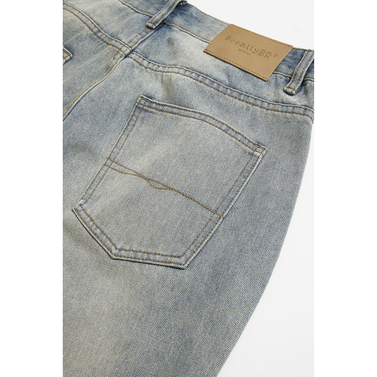 Close-up of light blue jeans showing a rear pocket, waistband stitching and a tan leather patch.
