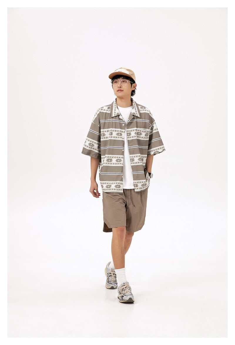Model wearing a brown-and-cream geometric striped short-sleeve shirt over a white tee with taupe shorts.