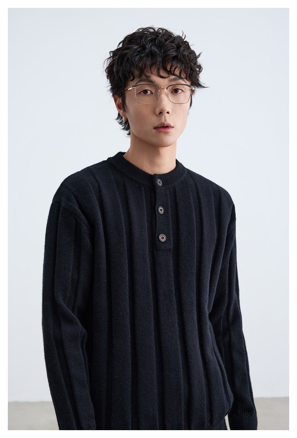 Close front view of a model wearing a black ribbed sweater with a crew neck and three-button placket.
