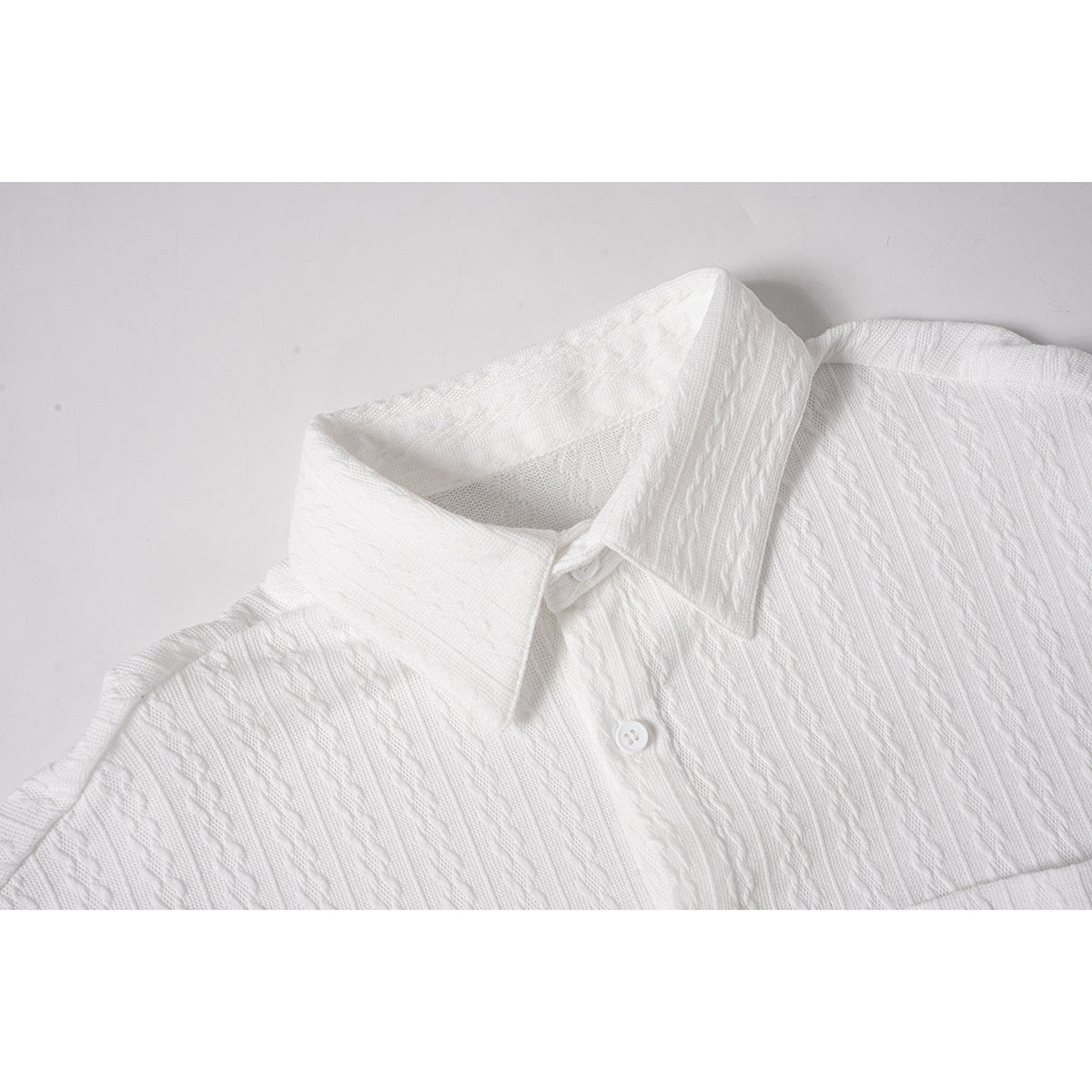 Close-up of a white short-sleeve shirt showing its pointed collar, button, and raised vertical knit pattern.