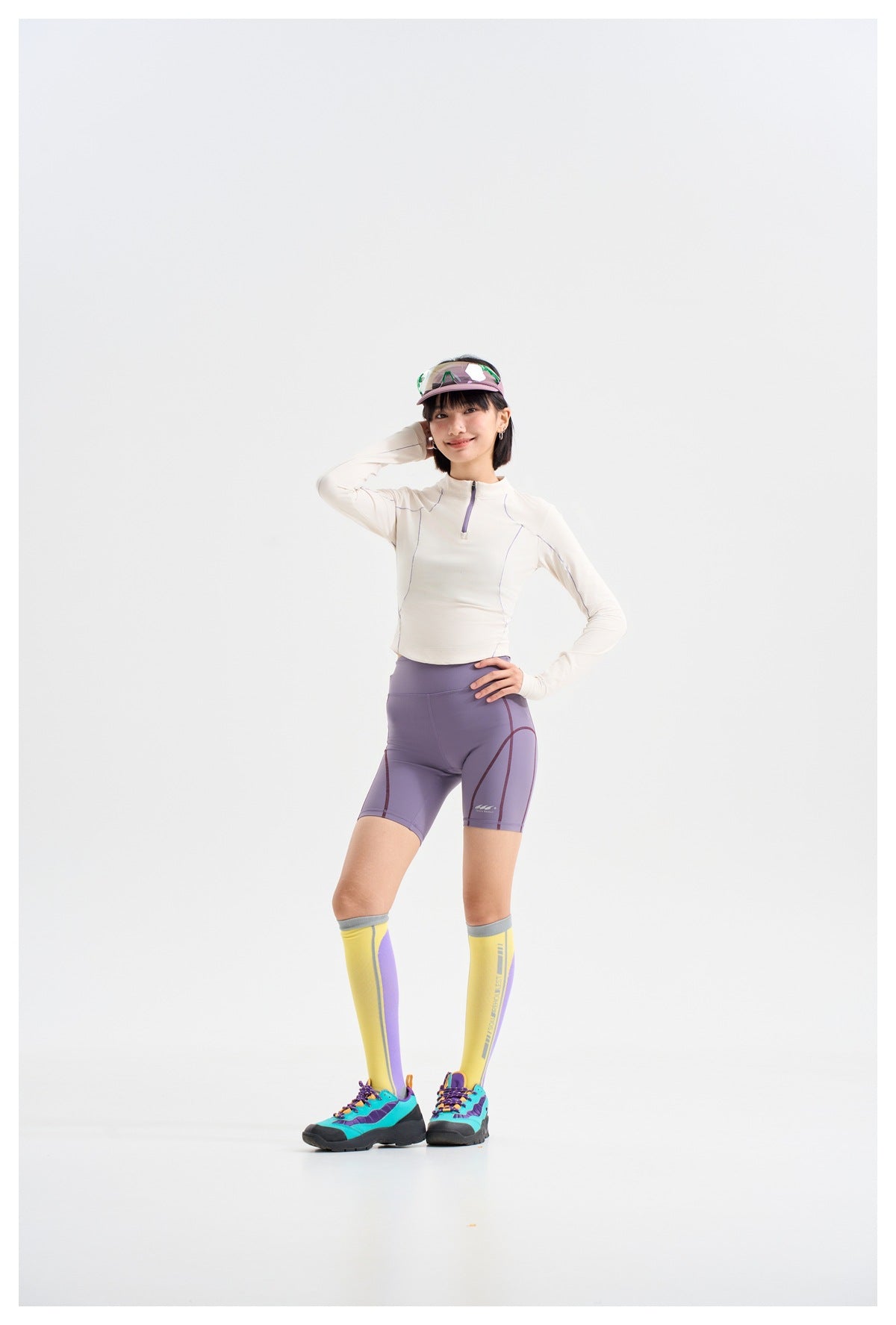 Model wearing a white long-sleeve quarter-zip top, lavender cycling shorts, and yellow knee-high socks.