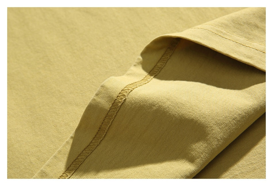 Close-up of pale yellow T-shirt fabric and an overlocked seam beneath a folded edge.