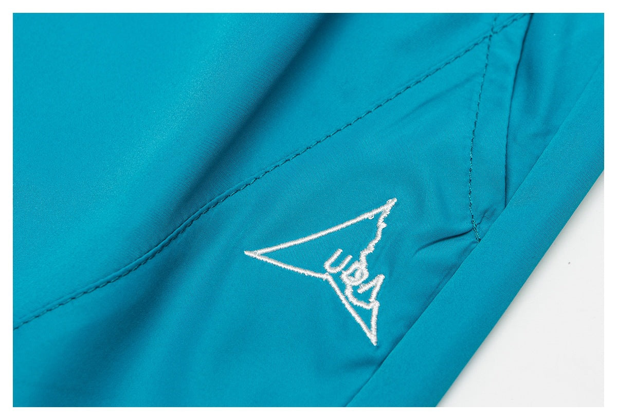 Close-up of a white embroidered triangular USA motif on turquoise shorts.