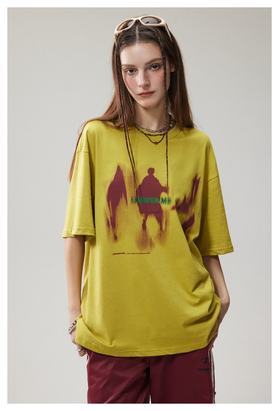 Model wearing a yellow oversized T-shirt with burgundy abstract graphics and green lettering.