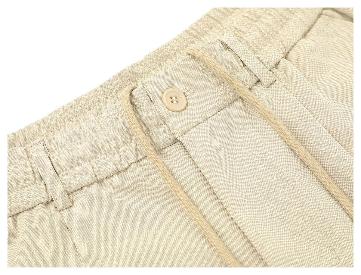 Close-up of the cream trousers' waistband with a button closure, belt loops and drawstrings.