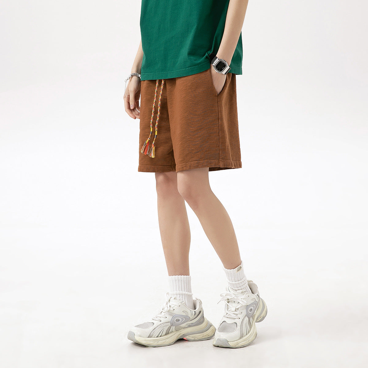 Angled view of a model wearing rust brown shorts with braided drawstrings and tassels.