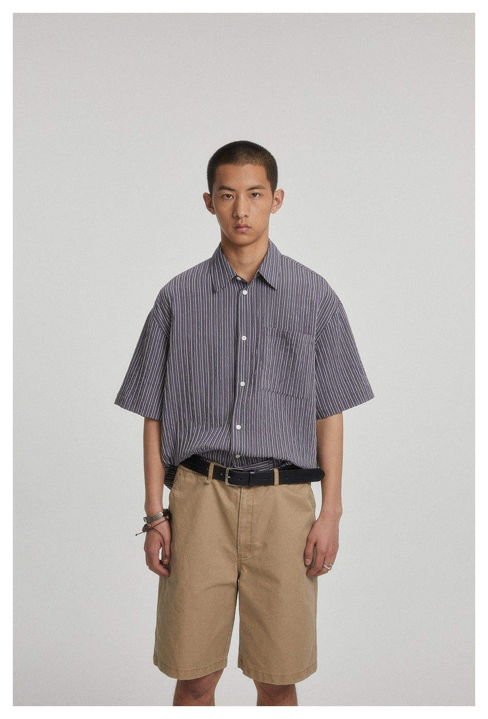 Front view of a model wearing a charcoal gray pinstriped short-sleeve button-up shirt and tan shorts.