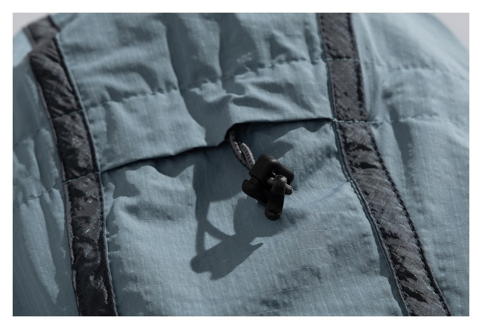 Close-up of a black cord toggle on blue-gray fabric between two dark accent strips.