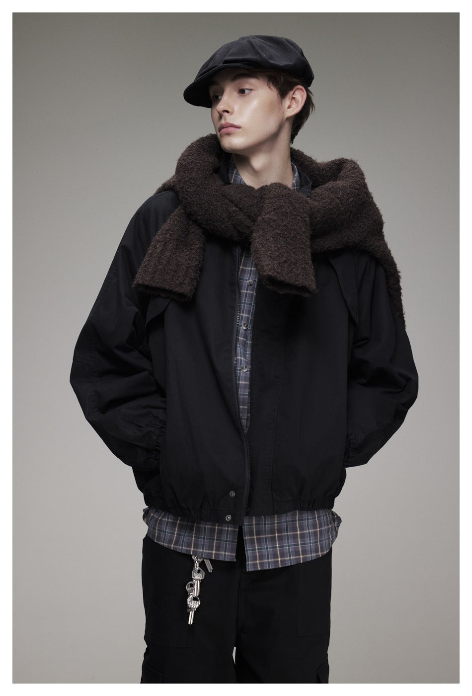 Closer view of a model in a black jacket over a plaid shirt, with a thick brown scarf and black cap.