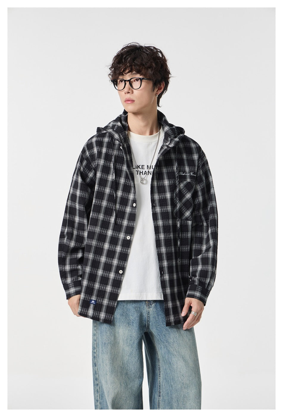 Model wearing an open black-and-white plaid hooded shirt over a white graphic tee and loose blue jeans.