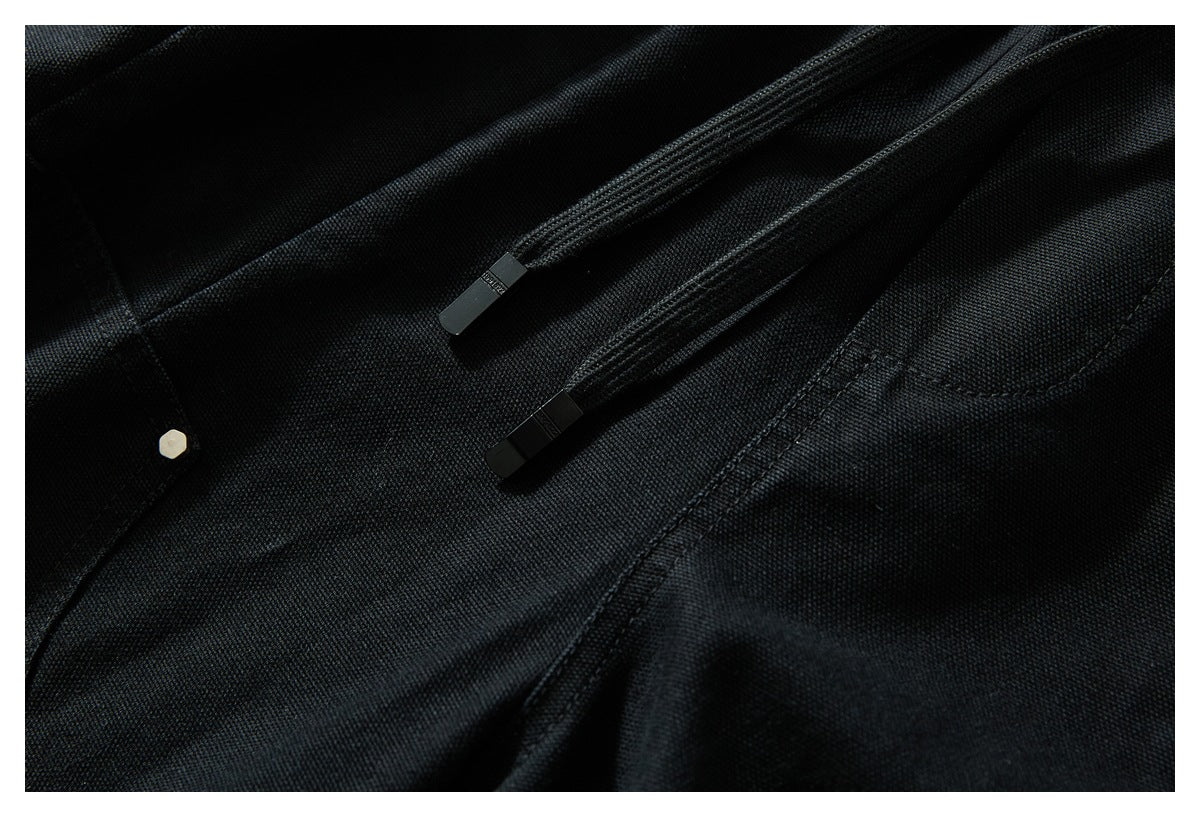 Close-up of black trousers with two black drawcord ends and visible stitching.