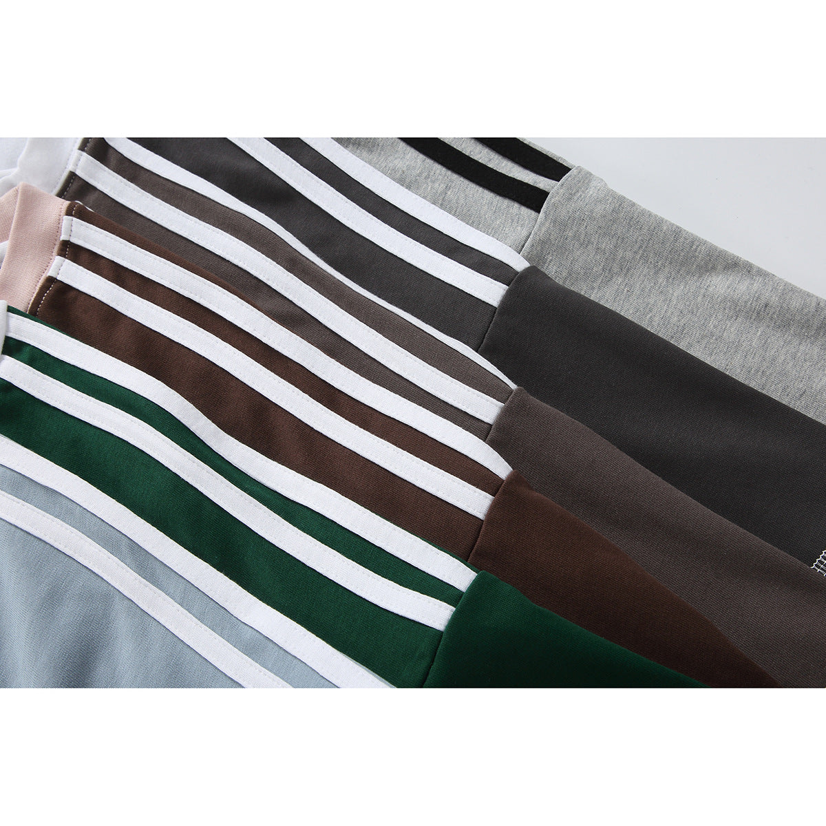 Close-up of overlapping T-shirts highlighting white double stripes on gray, brown, green, and blue sleeves.