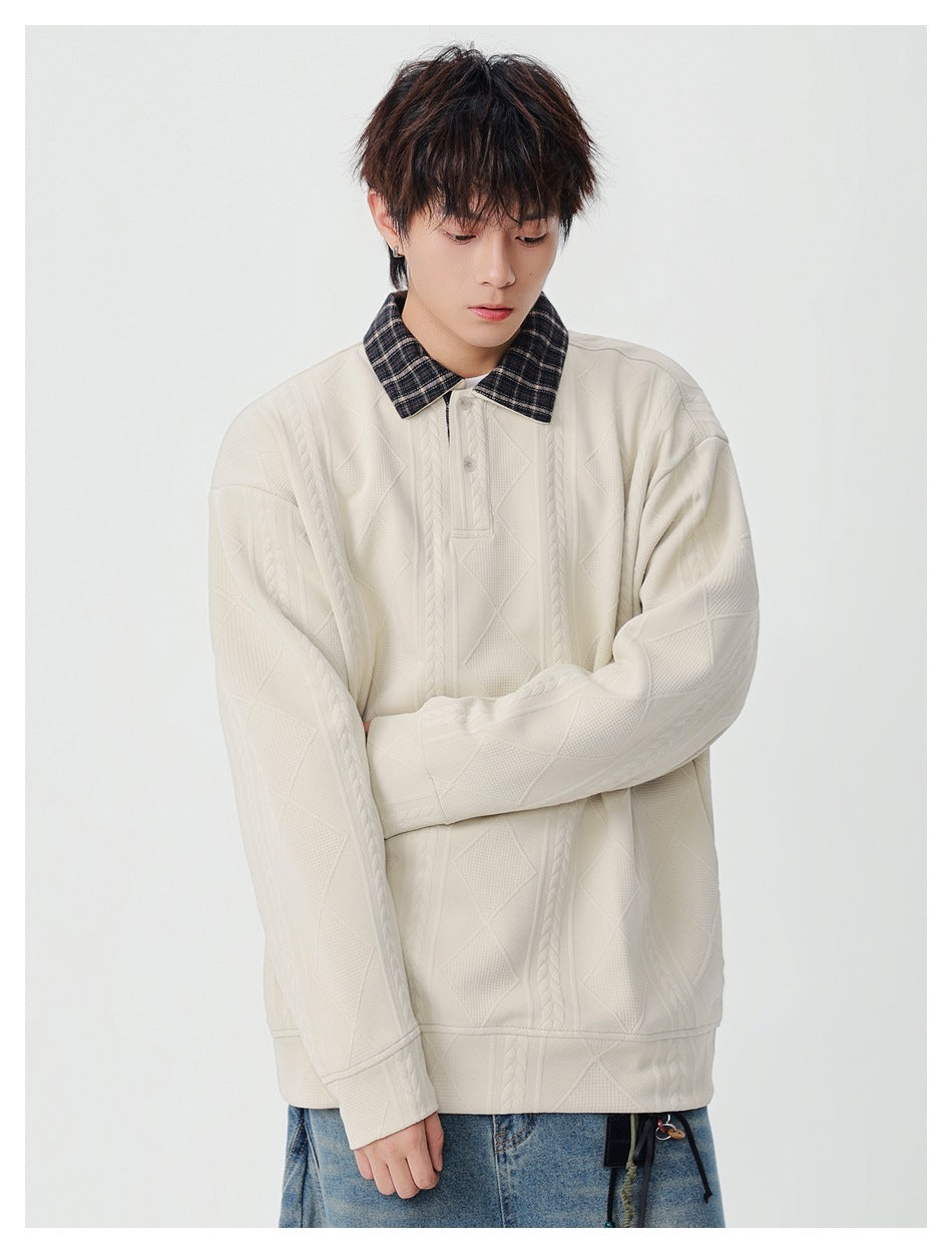 Model wearing an oversized cream pullover with a dark plaid collar, button placket, and raised cable and diamond patterns.