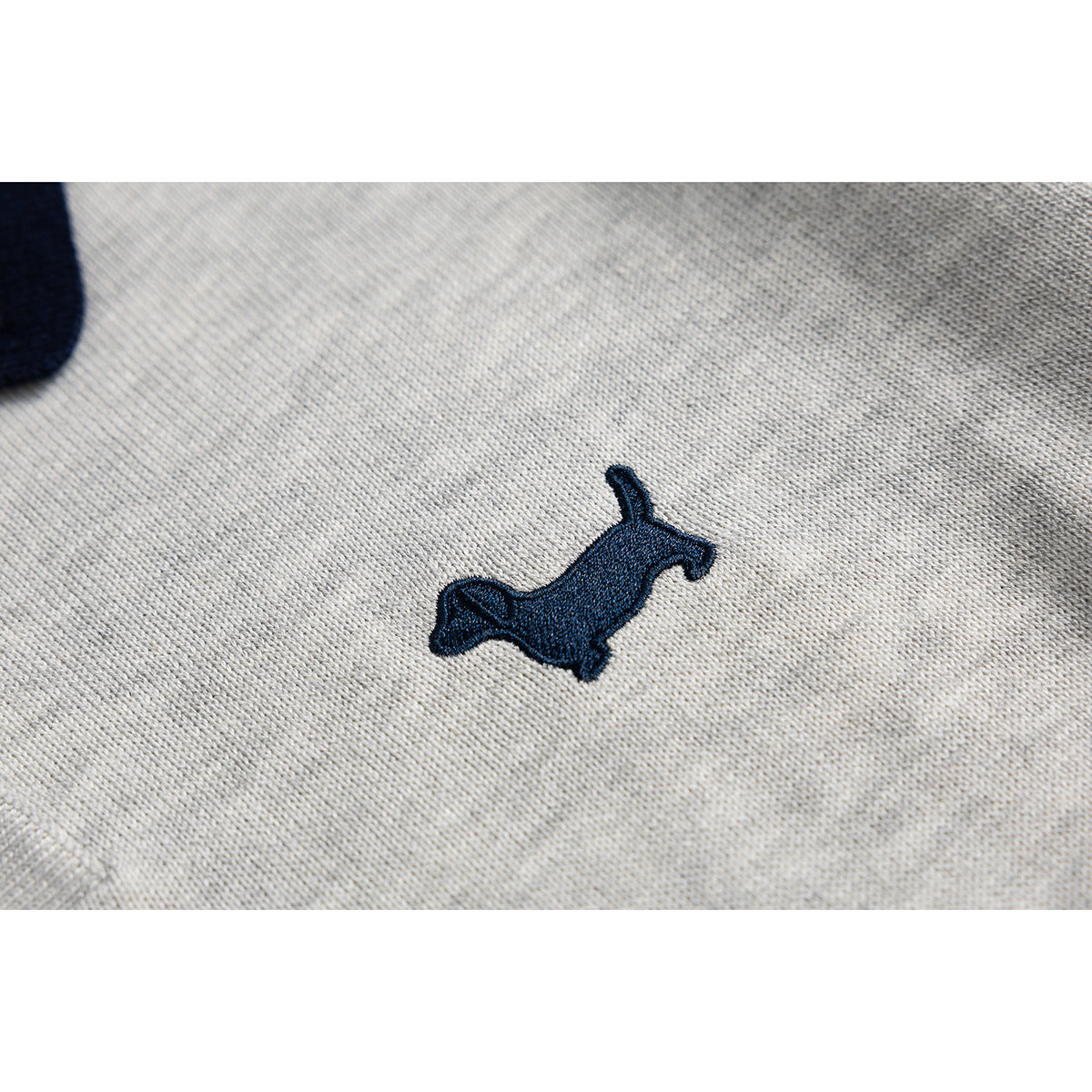 Close-up of a navy embroidered dog motif on light gray knit fabric.