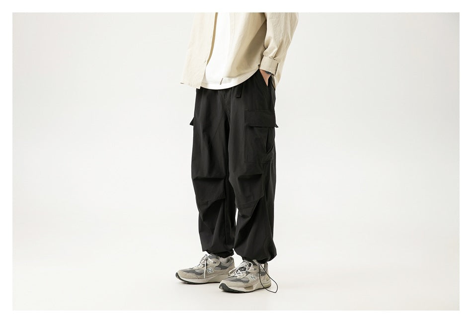 Front view of a model wearing loose black cargo pants with oversized thigh pockets and gathered hems.