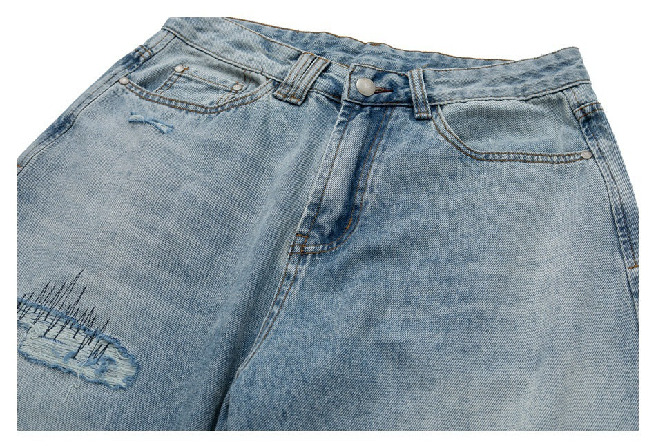 Close front view of light-wash jeans with curved pockets, a button waist, and a frayed thigh tear.