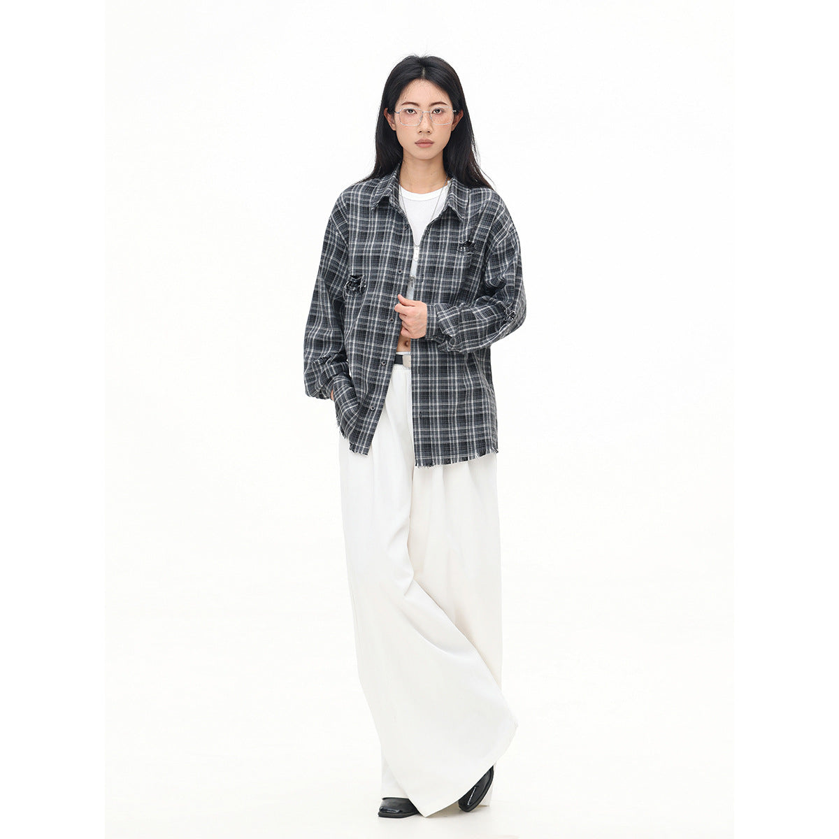 Full-length model wearing a charcoal gray plaid button-up shirt with distressed details and white wide-leg trousers.