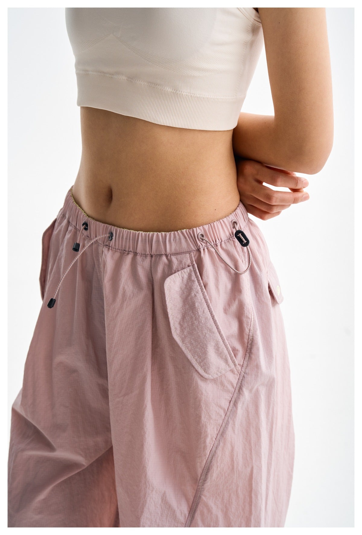 Close-up of light pink pants showing the elastic drawstring waistband, cord locks, and flap pocket.